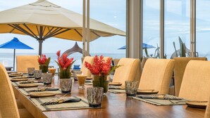 A dining area with a long table set for a meal, large windows, and two umbrellas.