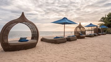 A beachside lounge area with wicker loungers and umbrellas, overlooking the sea.