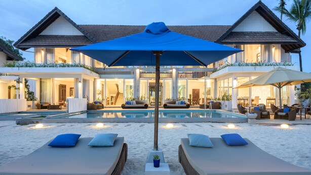 A resort with a swimming pool, lounge chairs, and a large umbrella.