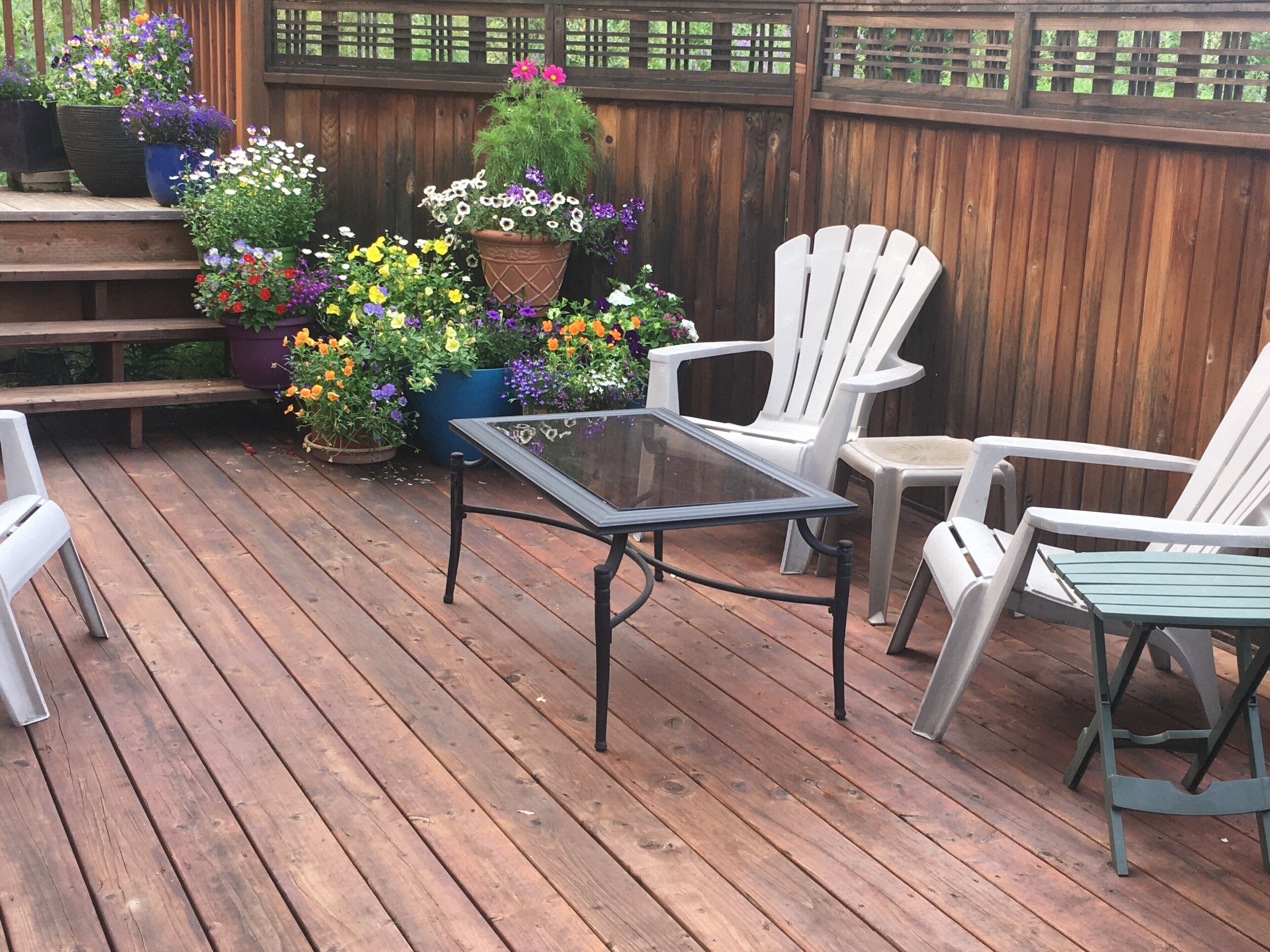 Une terrasse en bois avec une table à plateau de verre et des chaises Adirondack blanches.