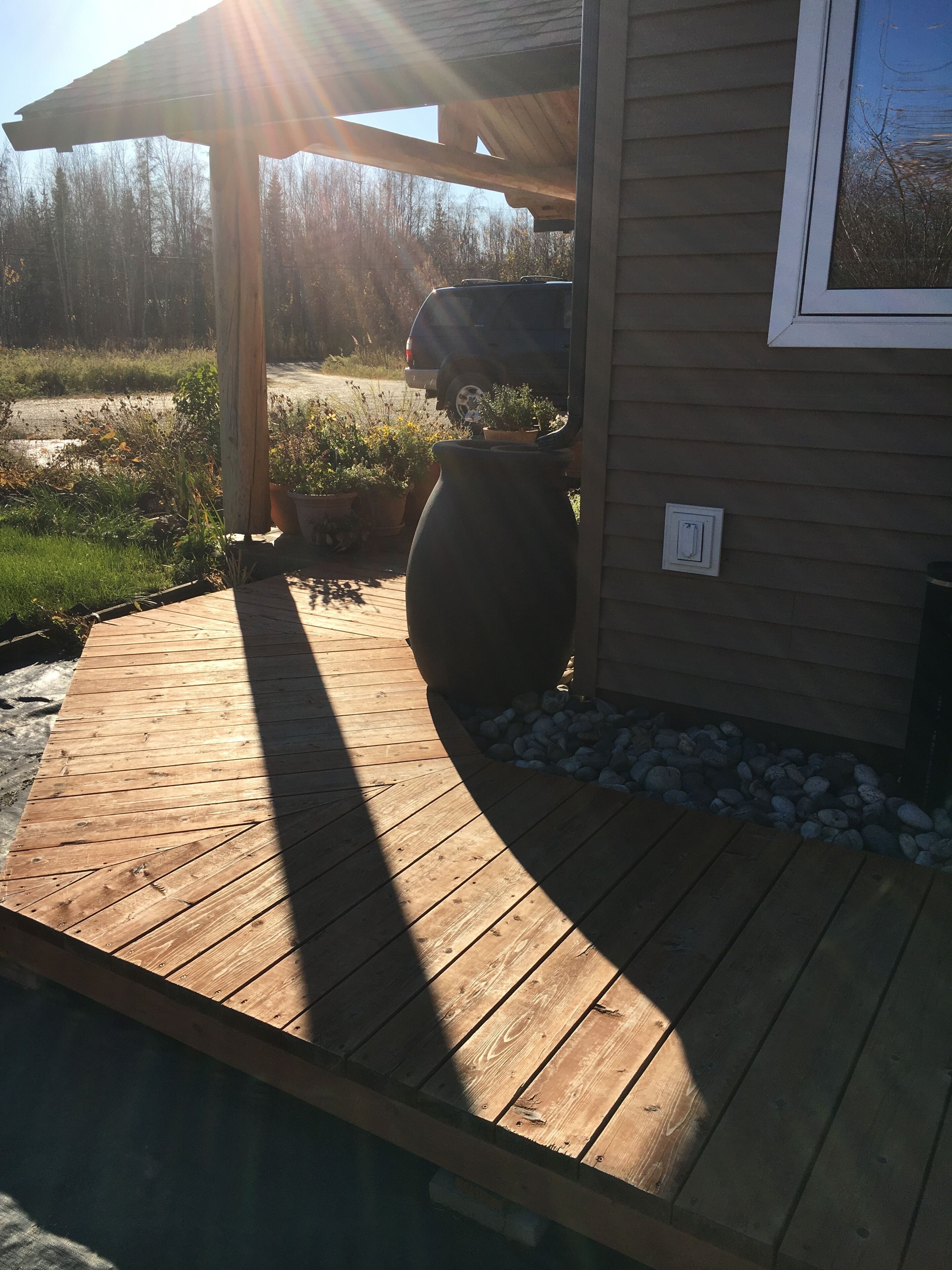 A wooden deck with a pergola, a large planter, and a small garden area.