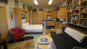 A compact living space with a bed, a red armchair, a black sofa, a small round table, and a bookshelf filled with books. - Cozy Studio apartment with a Courtyard  (North Pole)