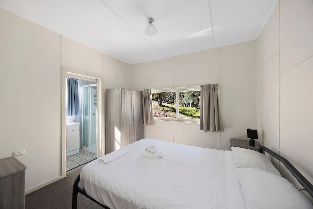 A hotel room with a bed, a bedside table, a window with curtains, and a view of the outdoors.