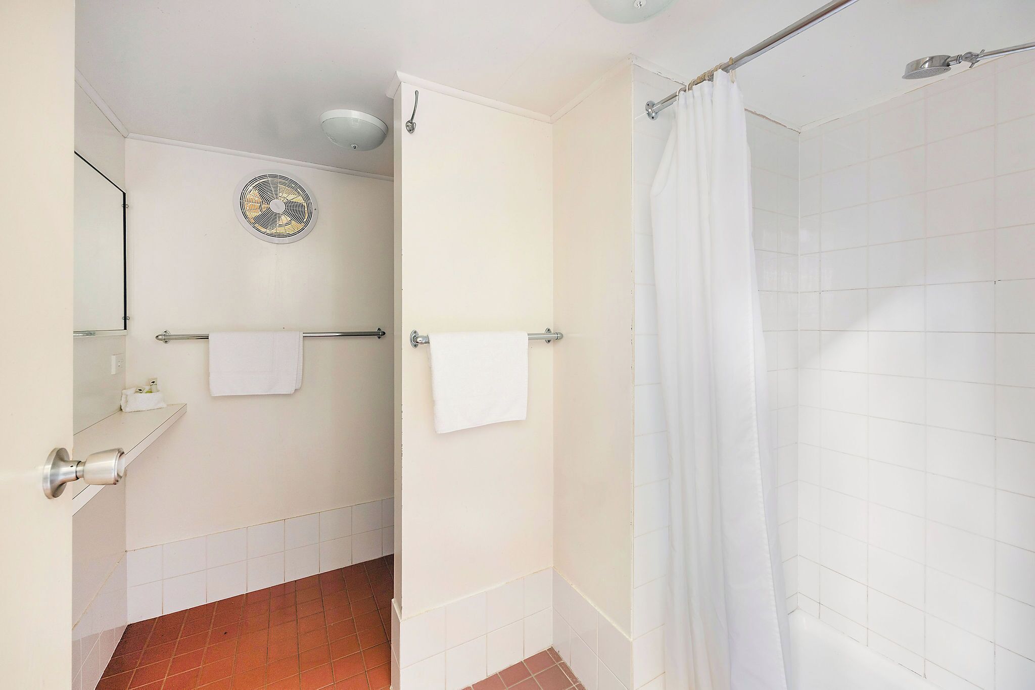 A bathroom with a shower, a towel rack, a fan, and a tiled floor.