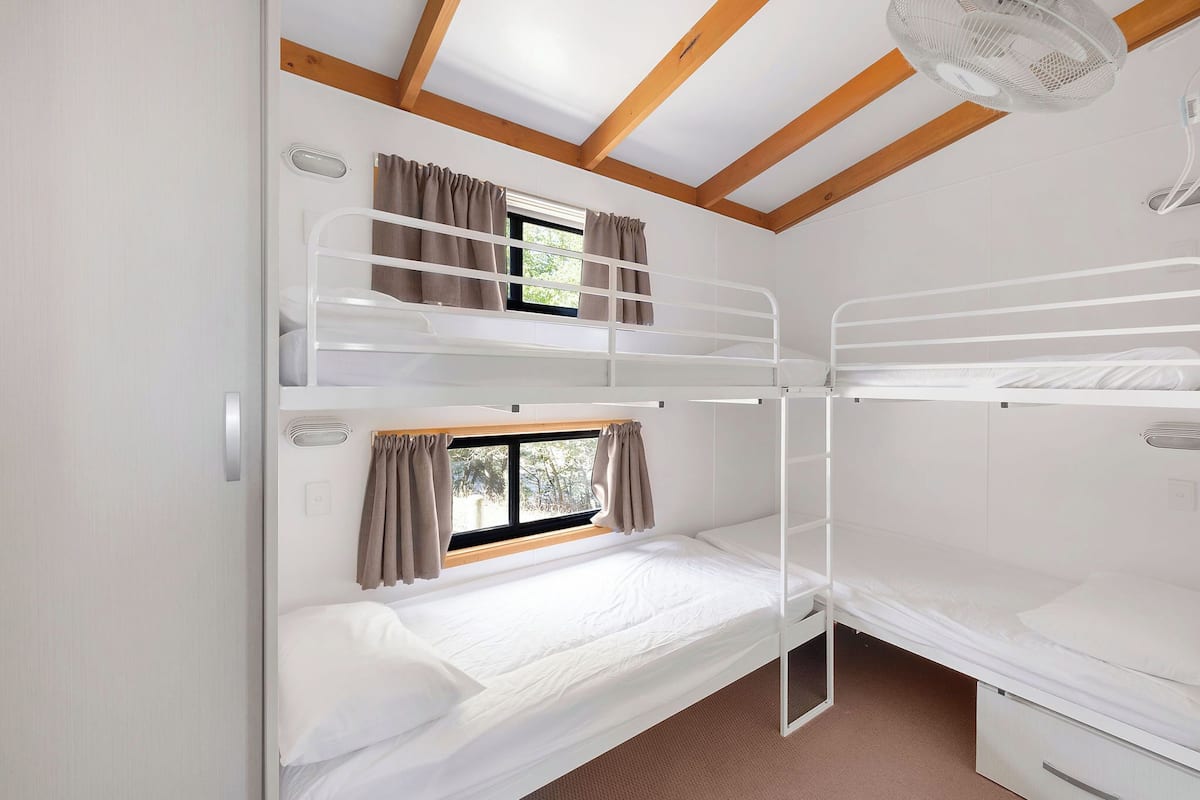 A bunk bed room with a window, curtains, and a ceiling fan.