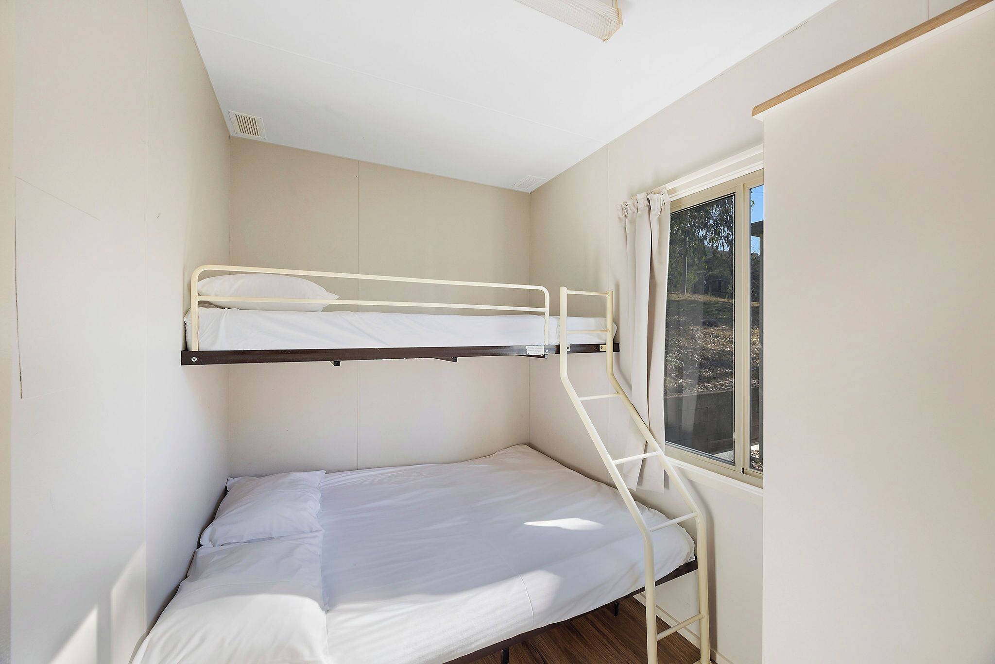 Een slaapkamer met een stapelbed, een raam, witte muren en een houten vloer.