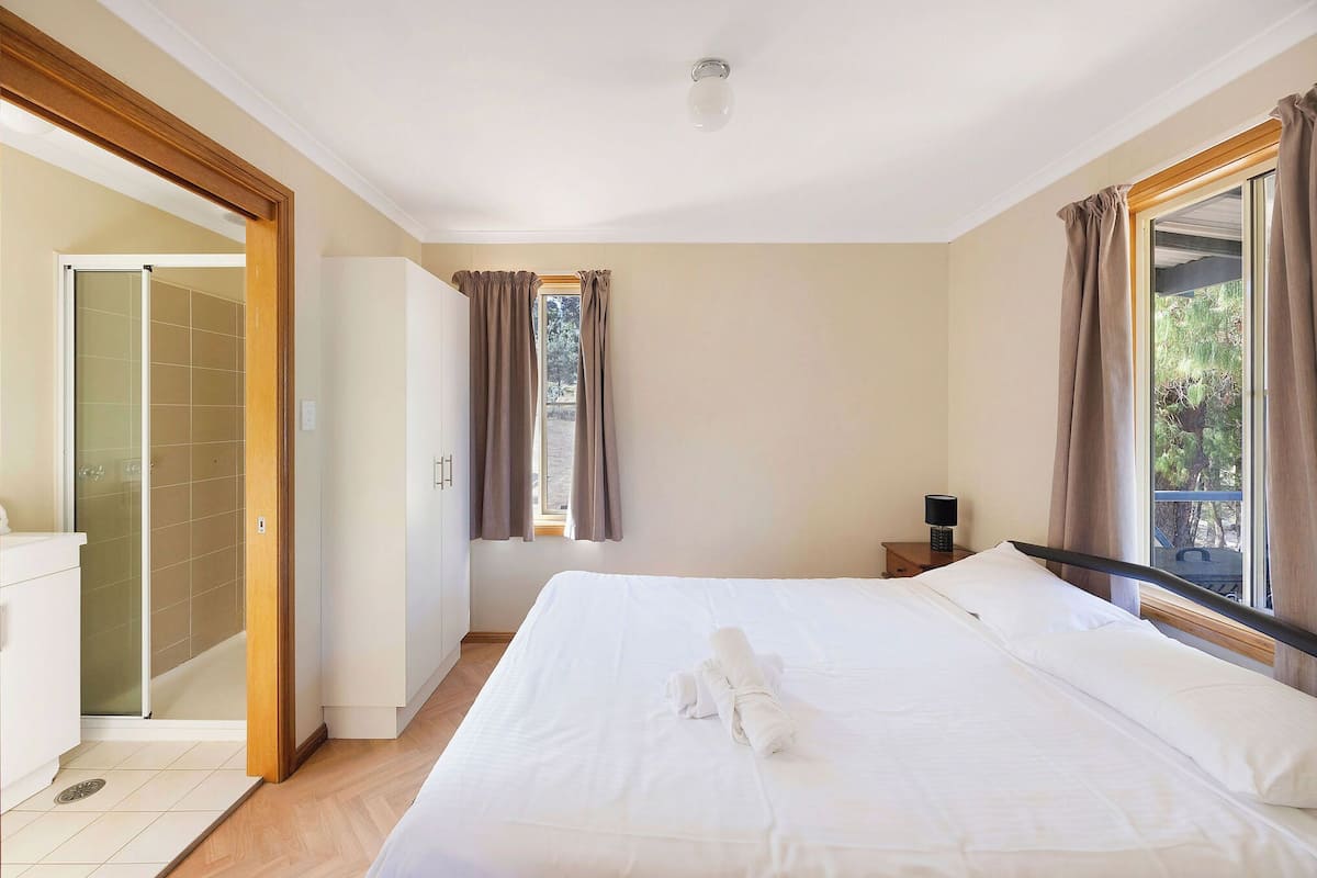 A hotel room with a large bed, a bedside table, a window with curtains, a shower area, and a view of the outdoors.