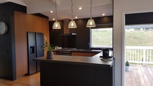 Moderni keittiö, jossa on tummat puukalusteet, keskellä oleva keittiösaareke, liesi ja riippuvalaisimet.