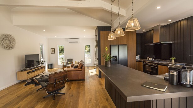 Moderni keittiö, jossa on tummat kaapistot, suuri keittiösaareke ja riippuvalaisimet.