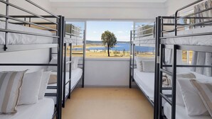 Un dormitorio con literas metálicas, ropa de cama blanca y vistas a un lago y árboles.