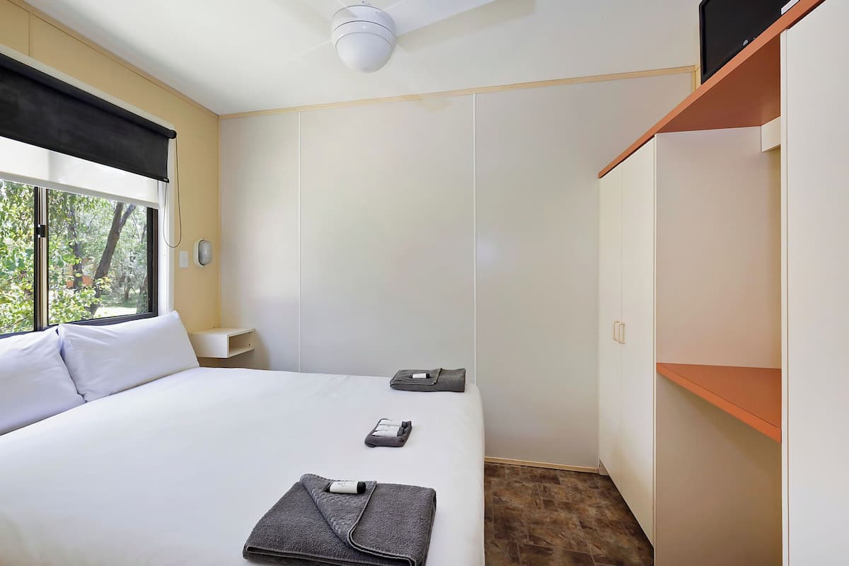 A hotel room with a bed, a bedside table, a wardrobe, and a window with a view of trees.