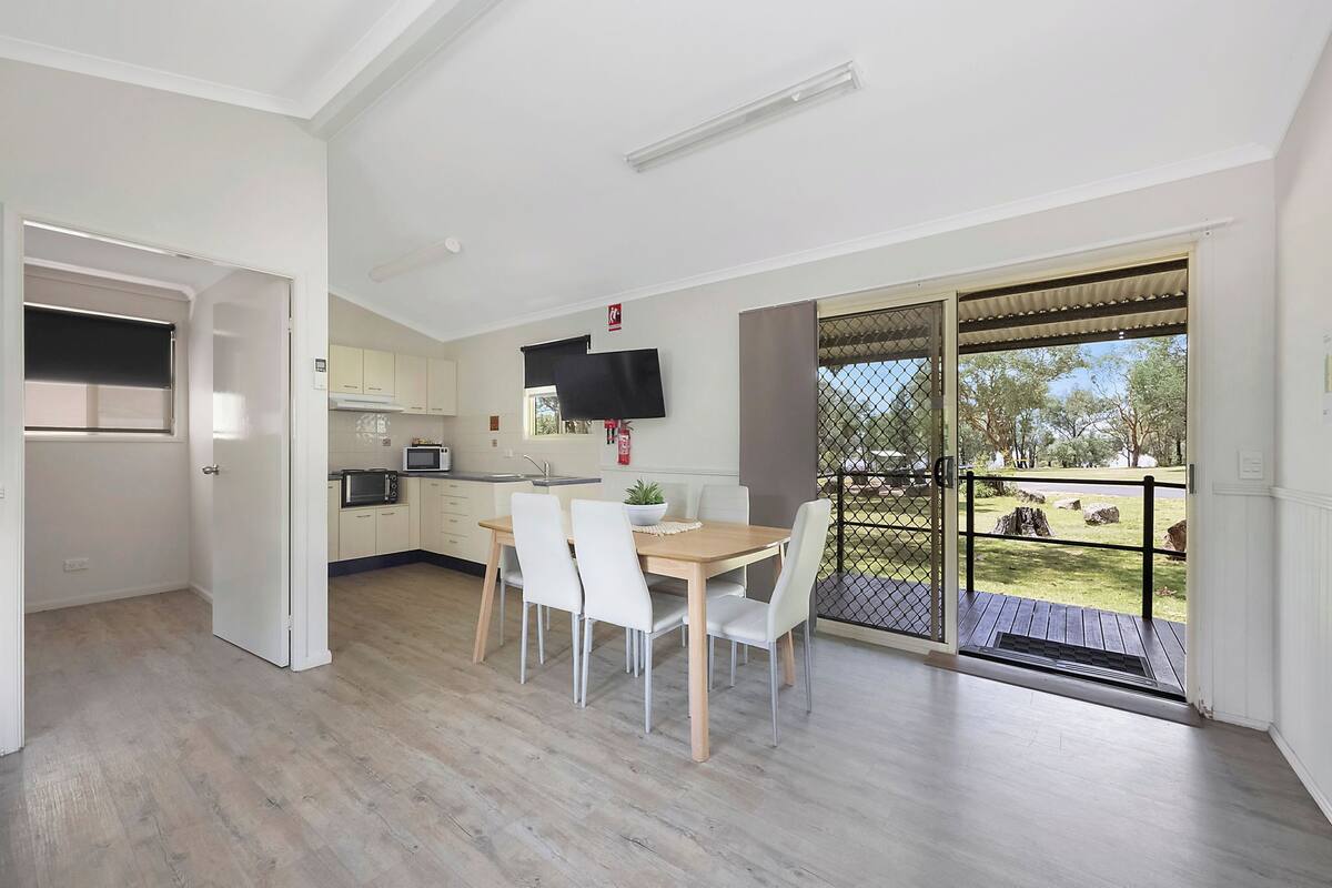 A modern kitchen with white cabinets, a wooden dining table, and a TV mounted above it.