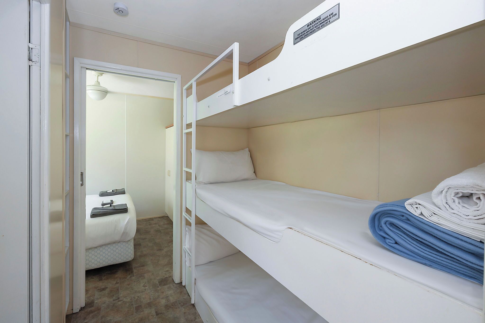 A bunk bed room with a white mattress, a ladder, and a warning label on the headboard.