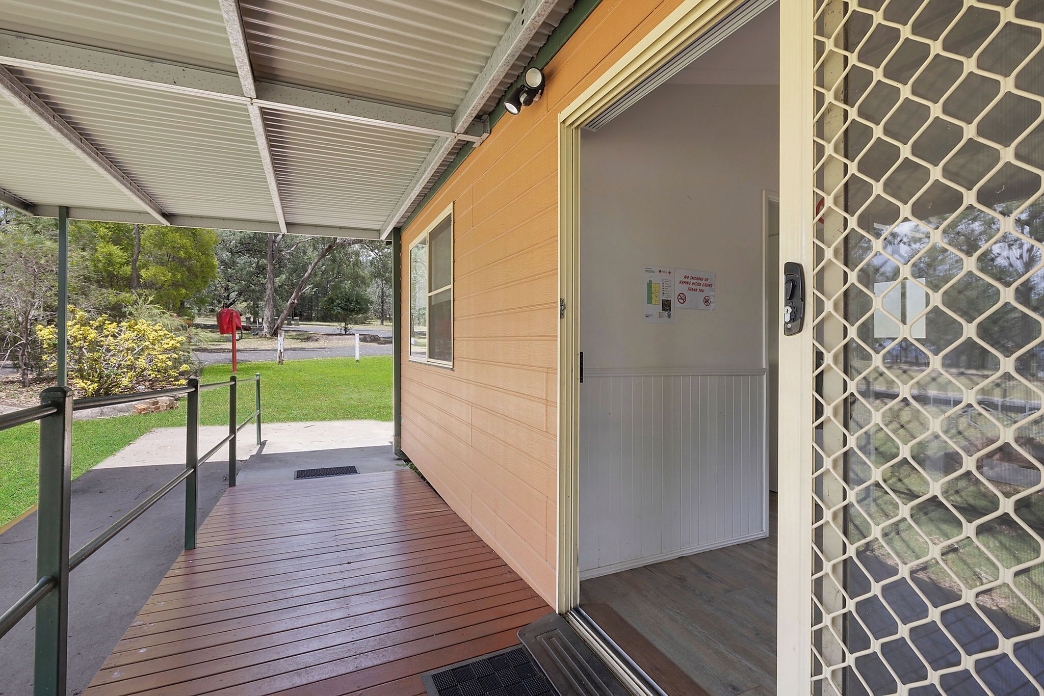 A covered outdoor area with a wooden deck, a metal railing, and a door with a security screen.