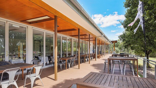 Un patio al aire libre con mesas y sillas de madera, grandes puertas de vidrio y techo de madera.