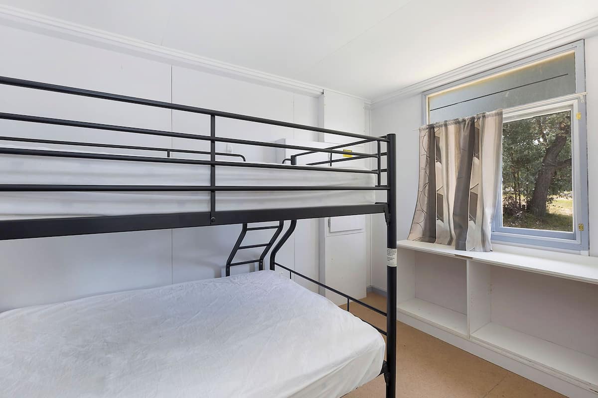 A bunk bed with a ladder, a window with curtains, and a white wall.