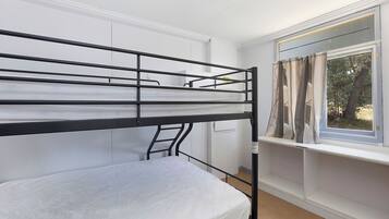 Una cama litera con escalera, una ventana con cortinas y una pared blanca.