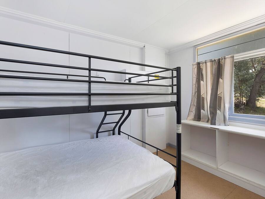 Una cama litera con escalera, una ventana con cortinas y una pared blanca.