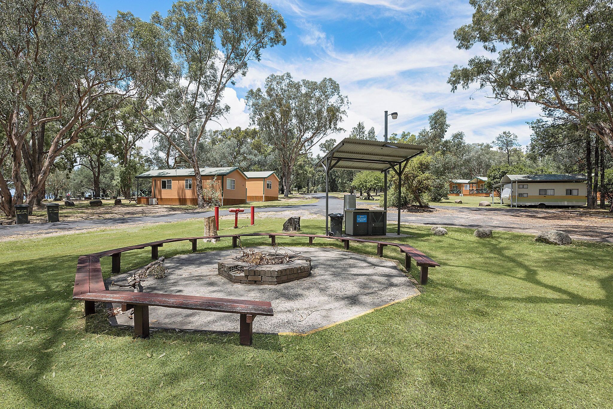 A park with a fire pit, picnic tables, and a covered seating area.