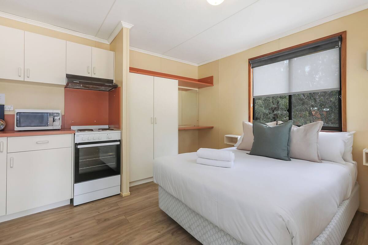 A bedroom with a bed, white cabinets, a microwave, and an oven.