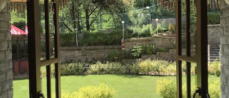 An open wooden door leading to a garden with a stone pathway, a pergola, and various plants.