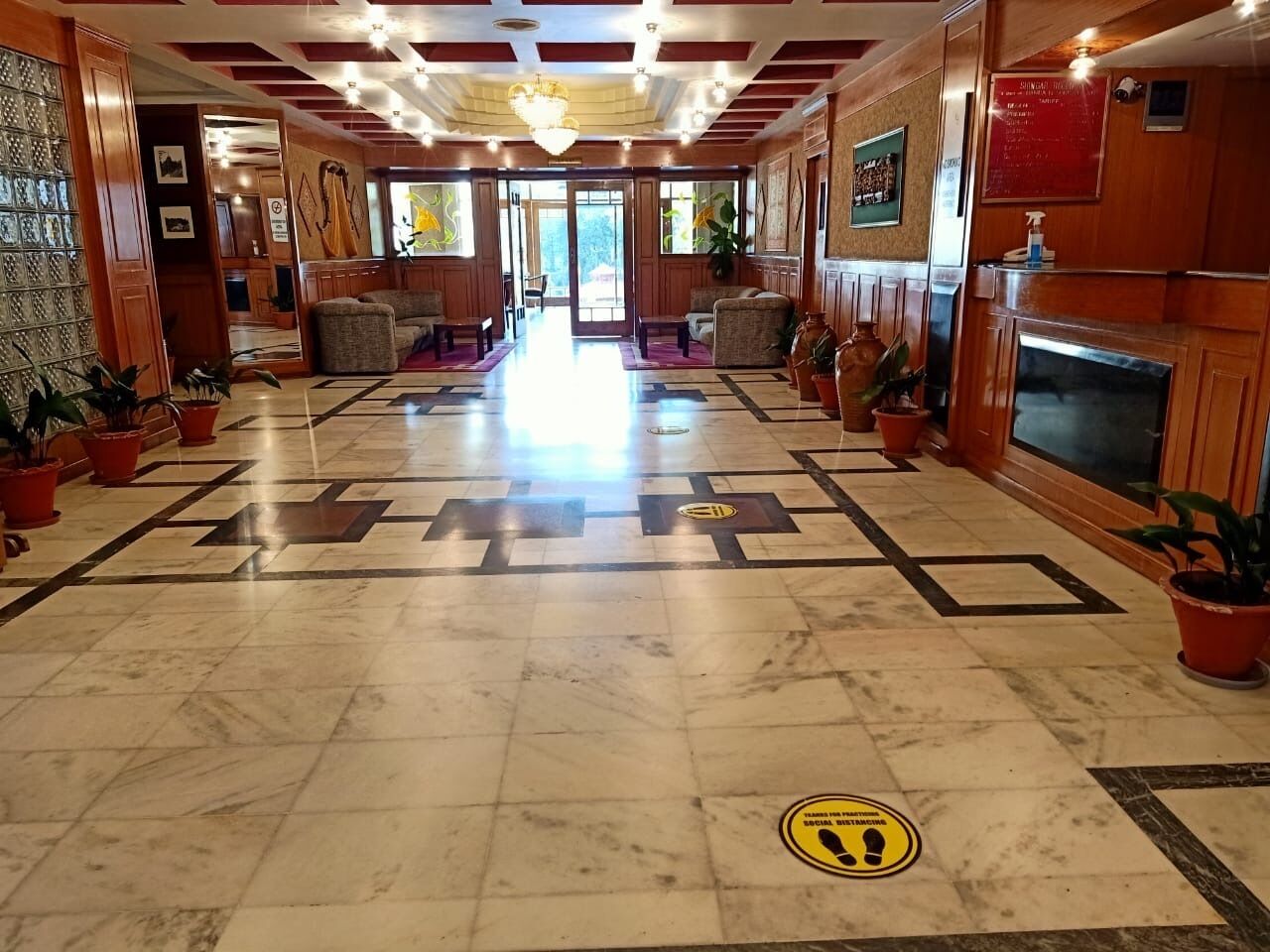 A hotel lobby with a marble floor, wooden paneling, and potted plants.