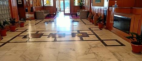 A hotel lobby with a marble floor, wooden paneling, and potted plants.