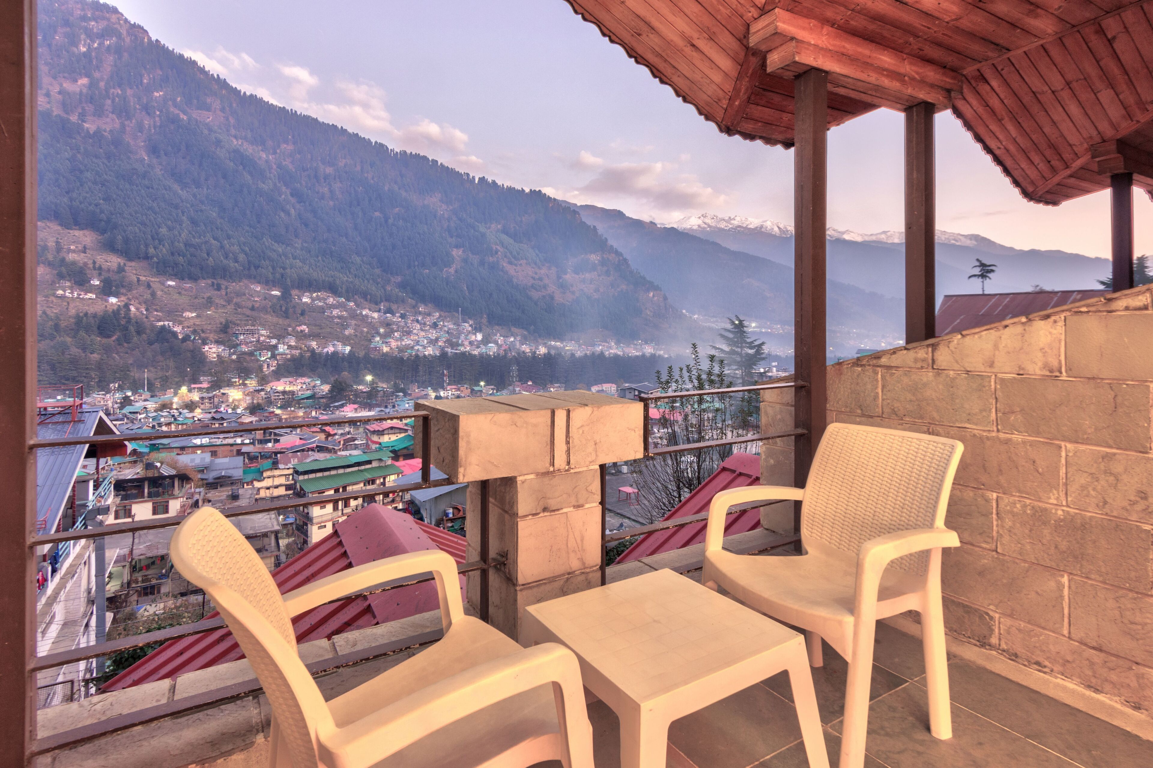 A balcony with two chairs and a table, overlooking a mountainous landscape with a village below.