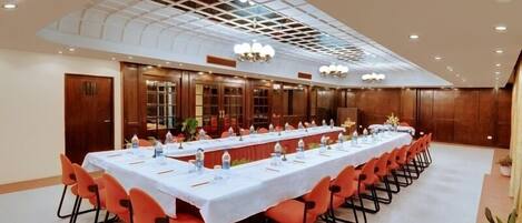 A conference room with a long table, orange chairs, and a ceiling with a grid pattern.