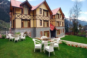 A chalet-style building with a stone facade and multiple windows, surrounded by a well-maintained lawn and outdoor seating area.