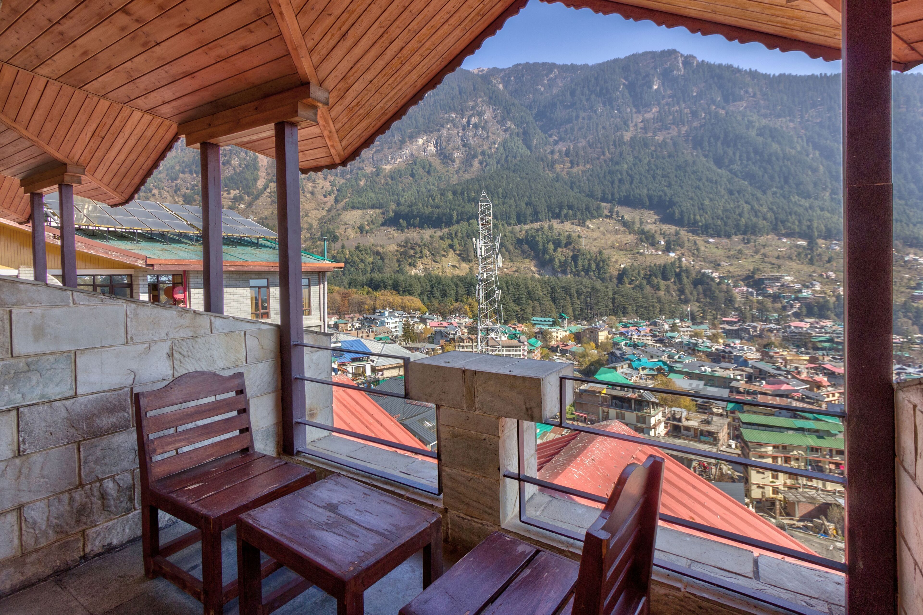 A wooden bench and table set under a roofed area with a view of a town and mountains in the background.