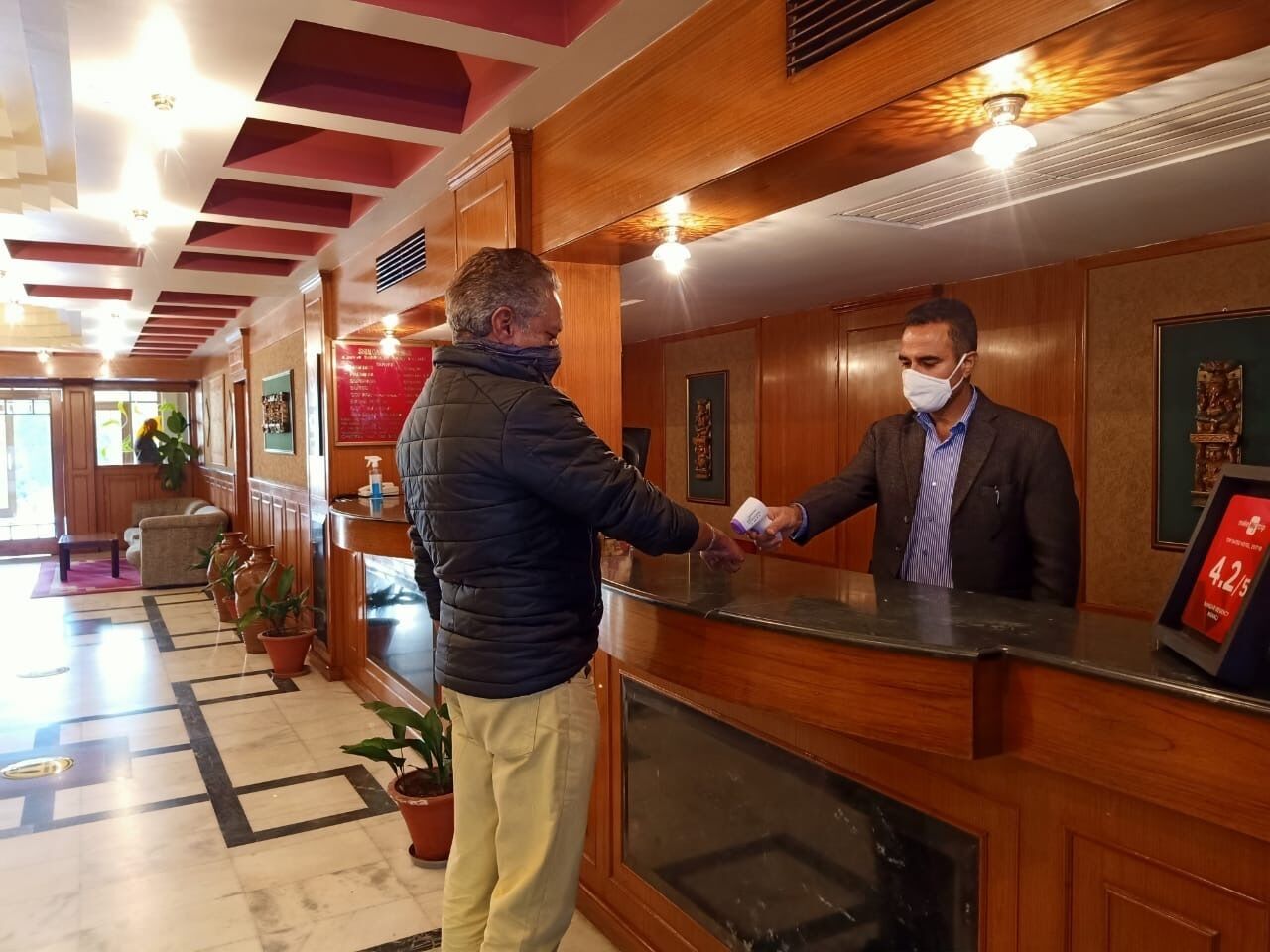 Un espace d’accueil d’hôtel avec un comptoir de réception en bois, des plantes en pot et un menu encadré accroché au mur.