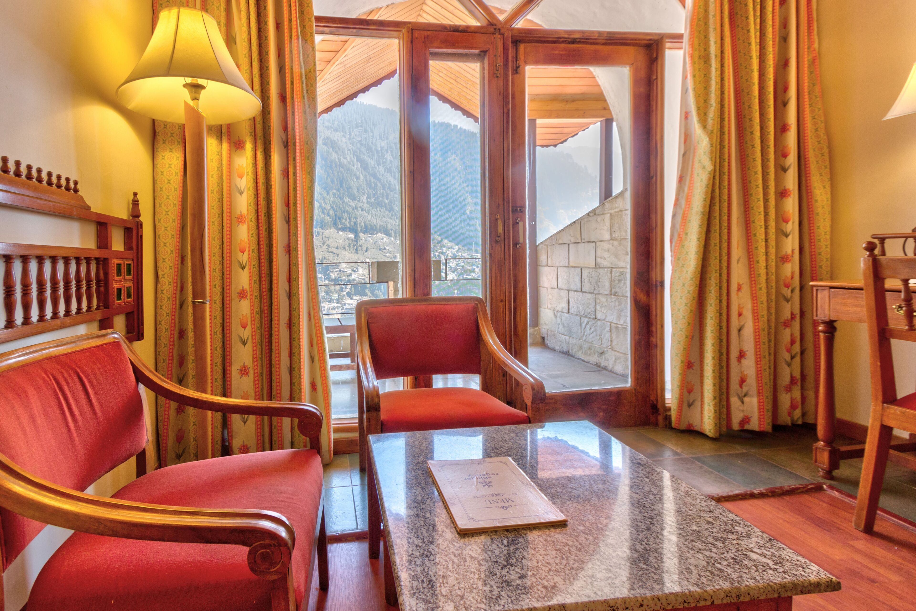 A room with a wooden chair, a table with a book, and a view of mountains through a glass door.