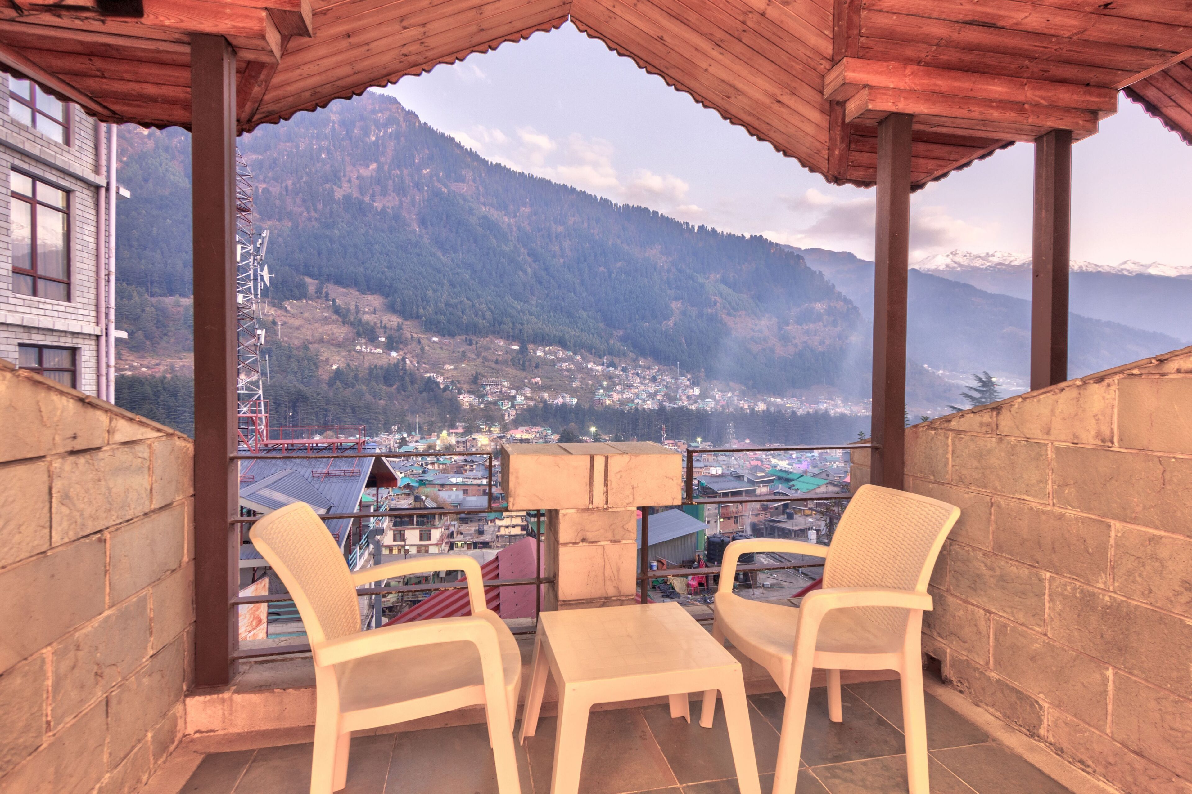 A balcony with two white plastic chairs and a table, overlooking a mountainous landscape with a town below.