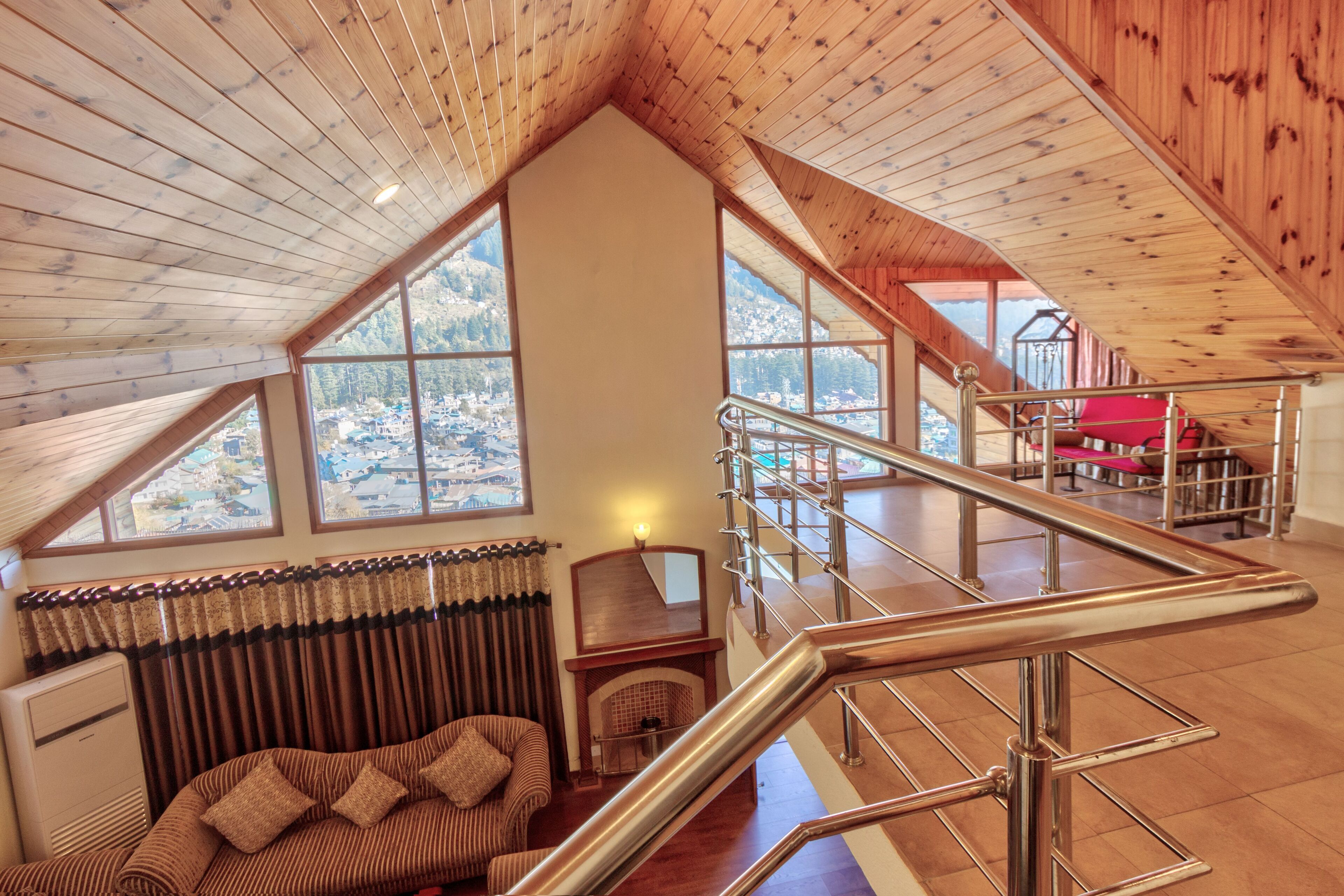A spacious loft with a high ceiling, large windows offering mountain views, a cozy seating area, and a metal staircase.