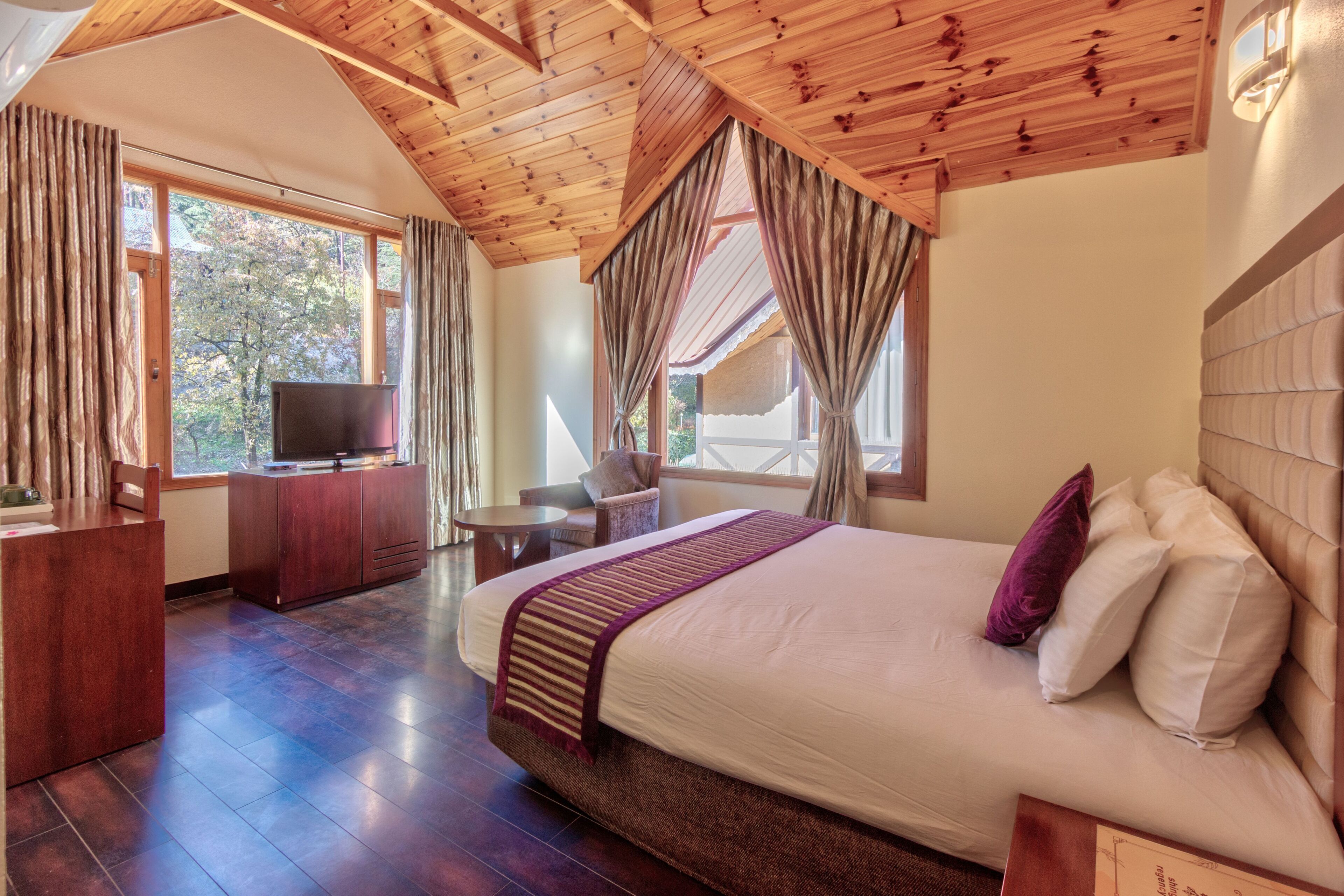 Une chambre avec un grand lit, un plafond en bois et un téléviseur posé sur une commode en bois.