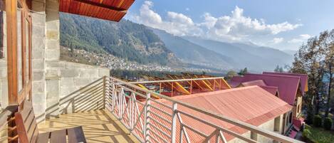 A balcony with a view of a mountainous landscape, a stone wall, and a red-roofed building.