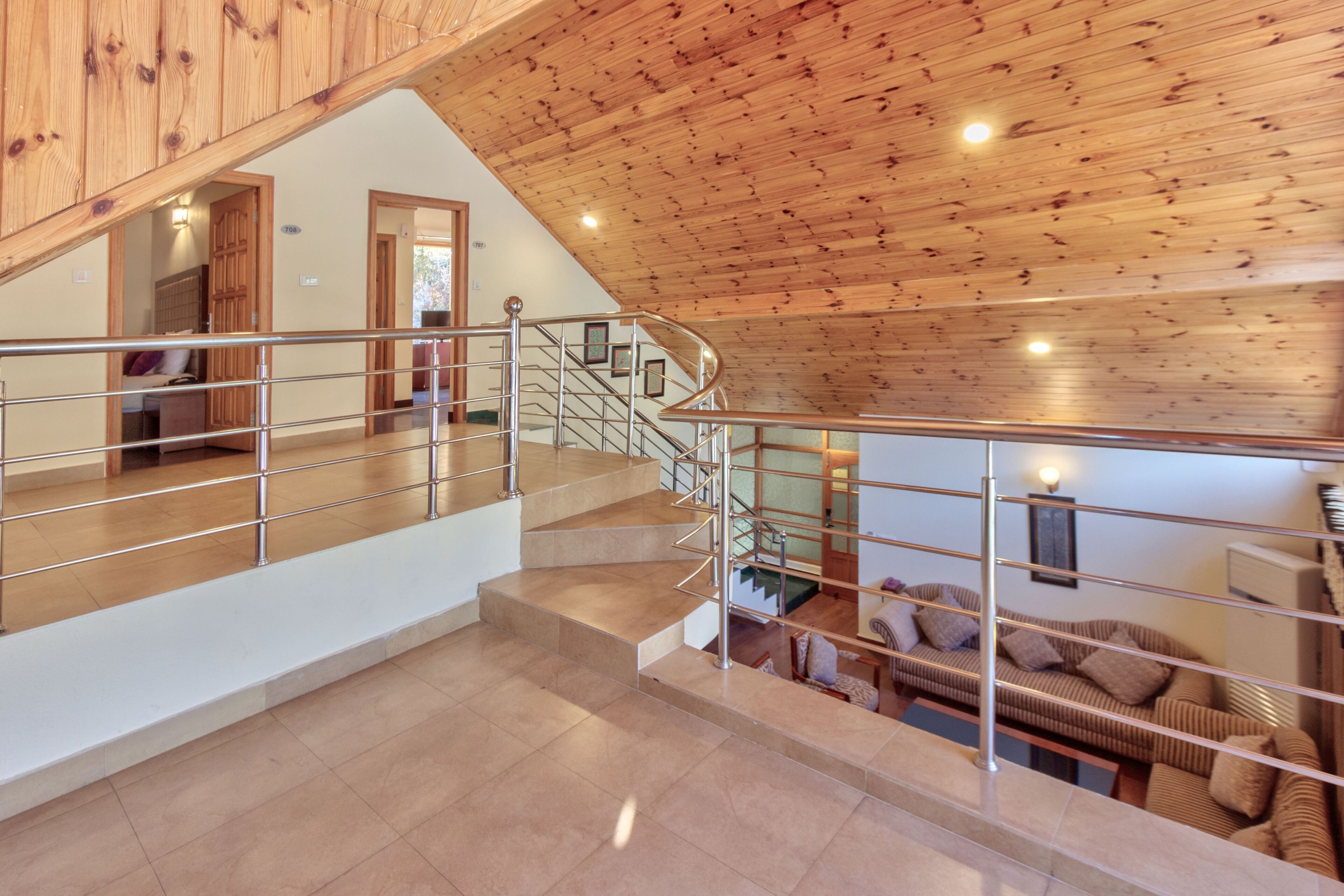 A modern interior with a wooden ceiling, a staircase with metal railings, and a living area with a sofa and cushions.