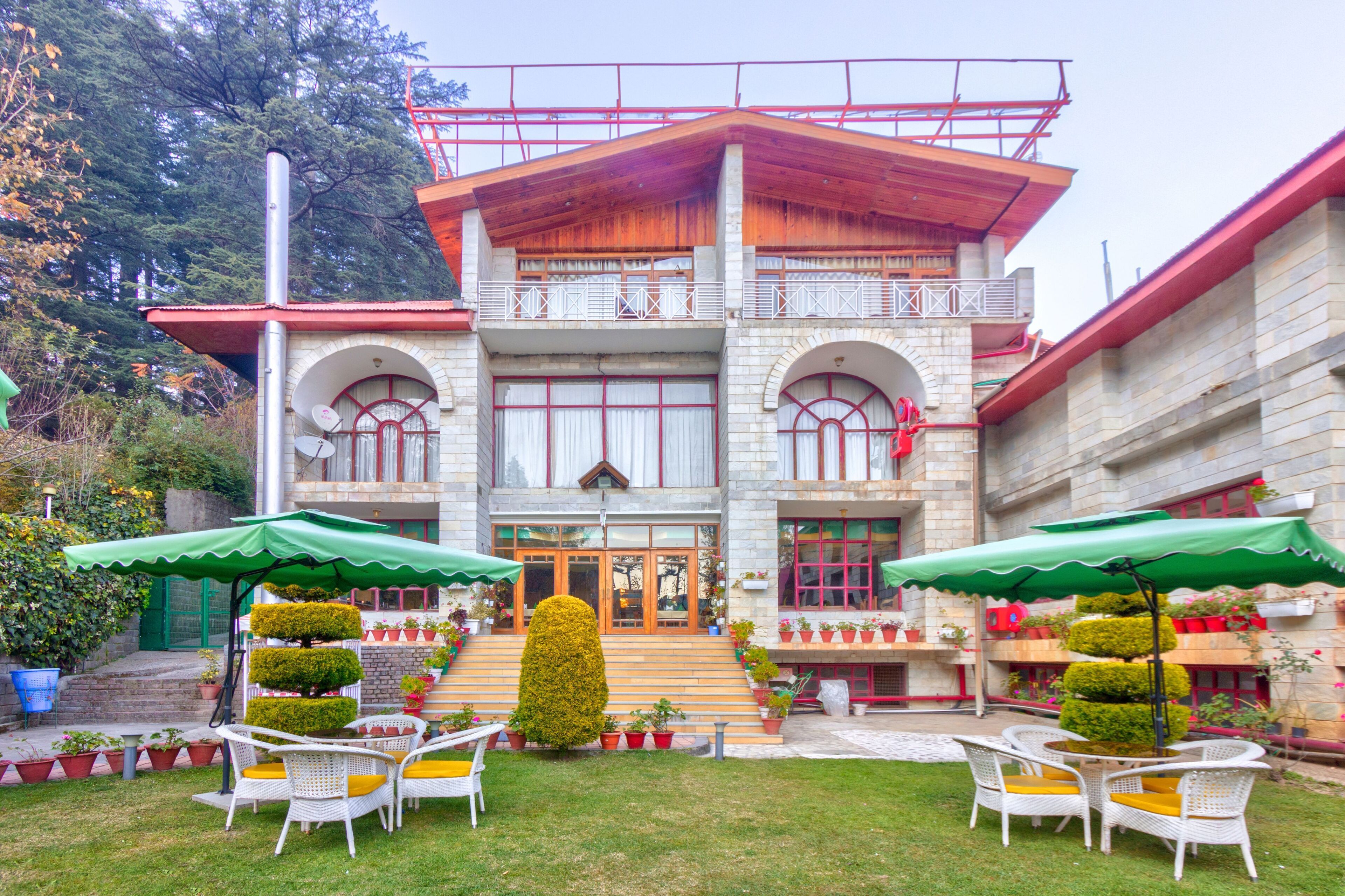 A building with a central entrance, multiple balconies, and outdoor seating with umbrellas.