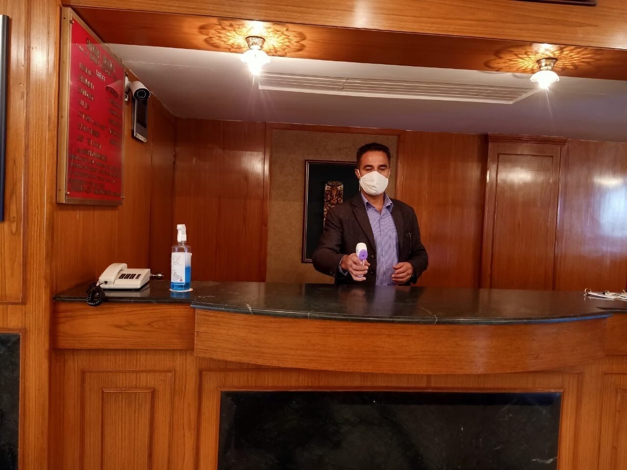 A wooden reception desk with a phone, a bottle of hand sanitizer, and a ceiling fan.