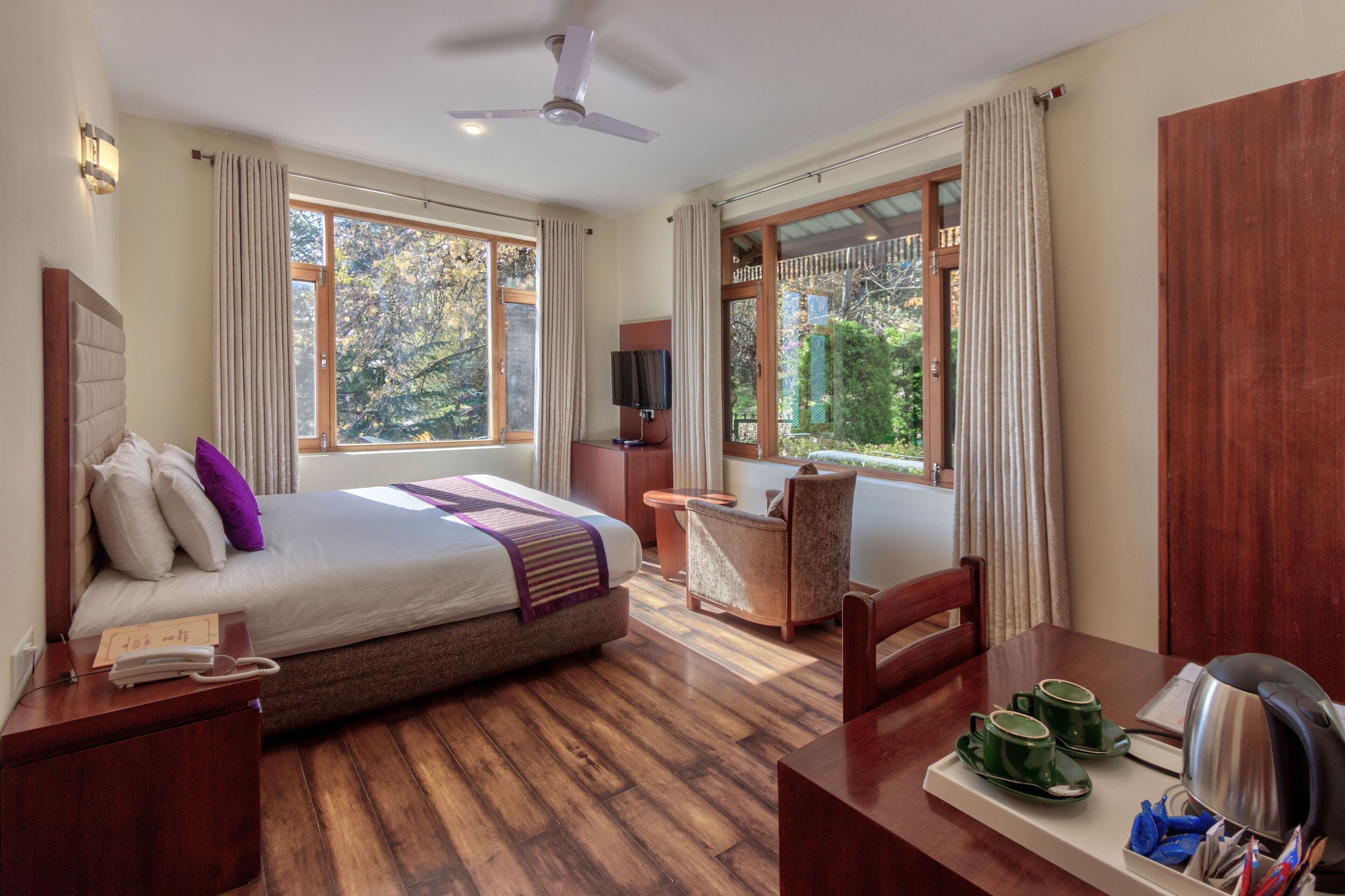 Habitación de hotel con cama, escritorio con tetera, silla y televisor.
