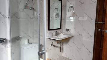 Une salle de bain dotée d’une douche à parois de verre, de toilettes, d’un lavabo avec un miroir au-dessus et de murs aux motifs de marbre.