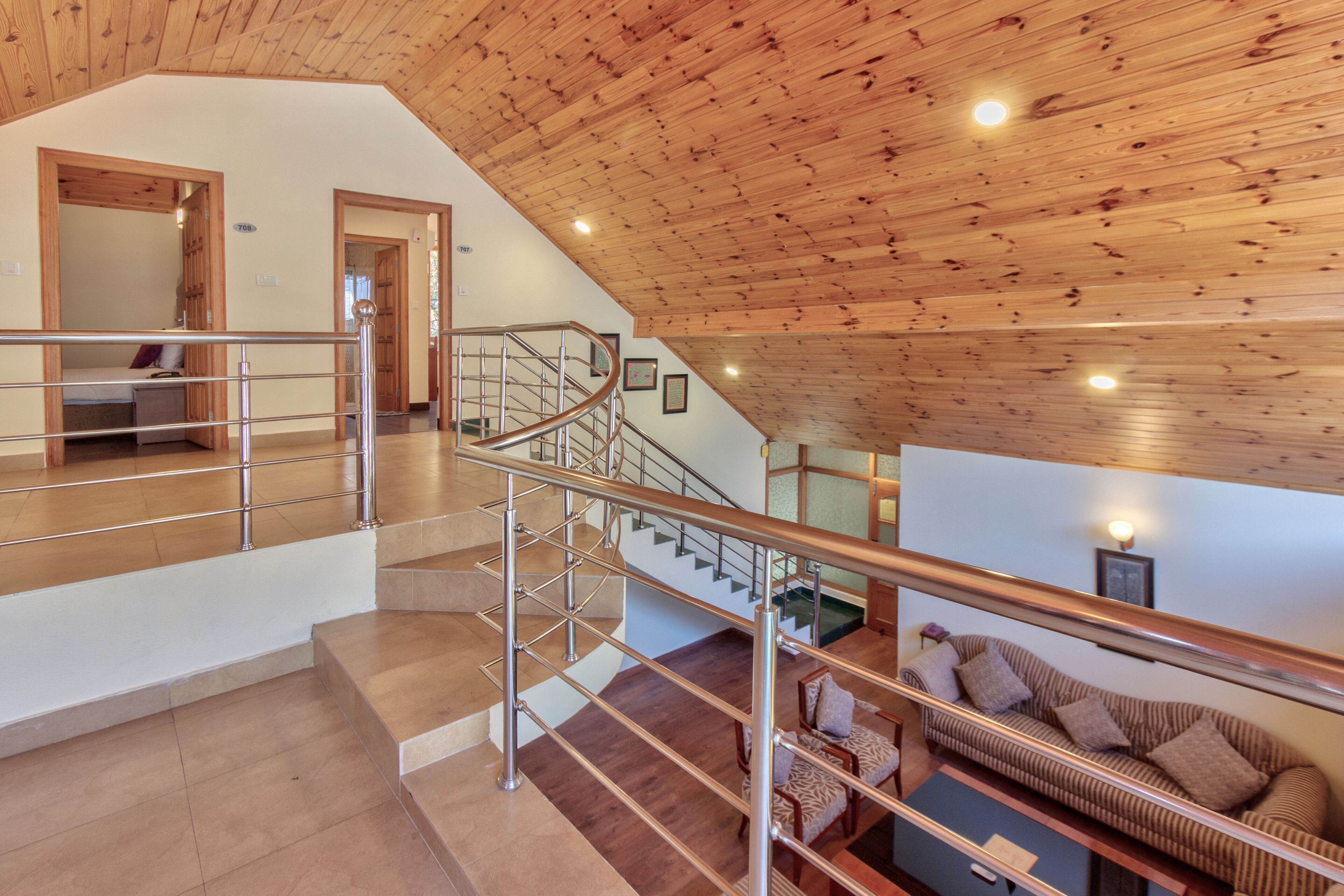 Un interior espacioso con techo de madera, una escalera con barandillas de metal y una sala de estar con sofá y cojines.