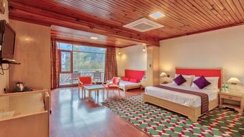 A hotel room with a wooden ceiling, a large bed with red and white bedding, a desk with a chair, a small table, and a view of the outdoors through a large window.
