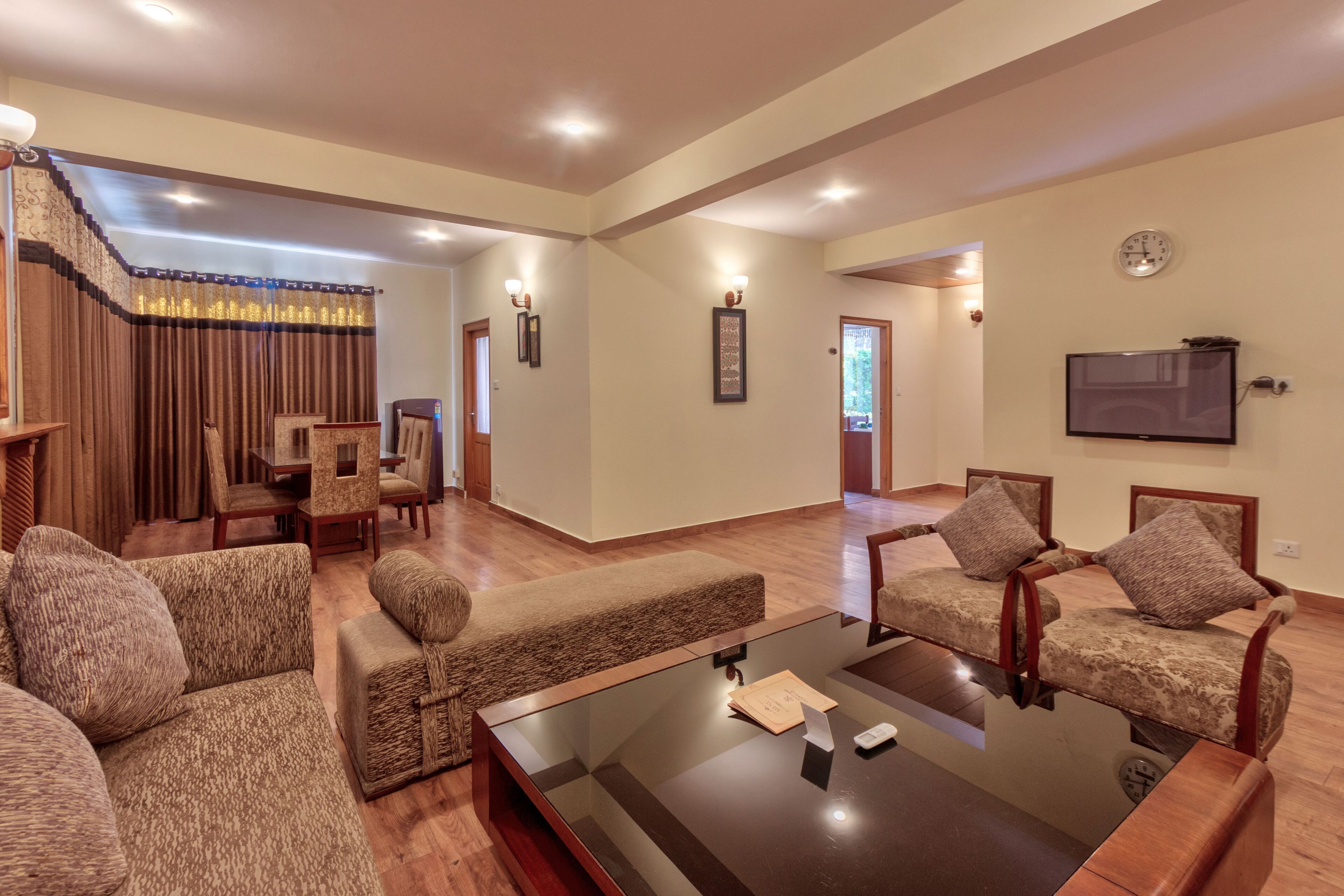 A spacious living room with a large glass coffee table, multiple sofas, and a dining area with a staircase.