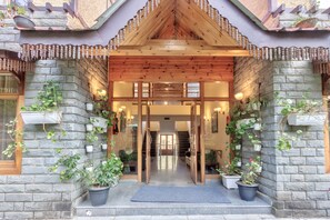 A stone building with a wooden entrance, potted plants, and a staircase leading inside.