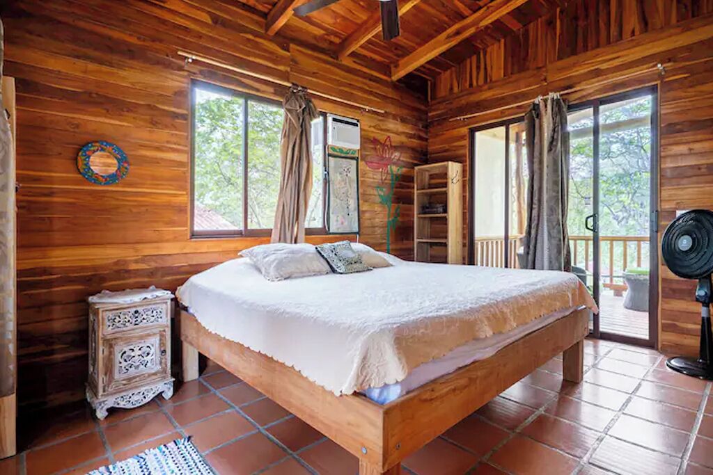 Una habitación de madera con una cama, una mesita y un ventilador.