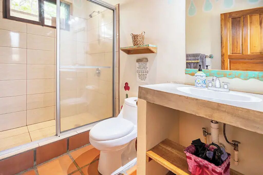 Een badkamer met een glazen douchecabine, een wit toilet en een wastafel met een houten aanrechtblad.