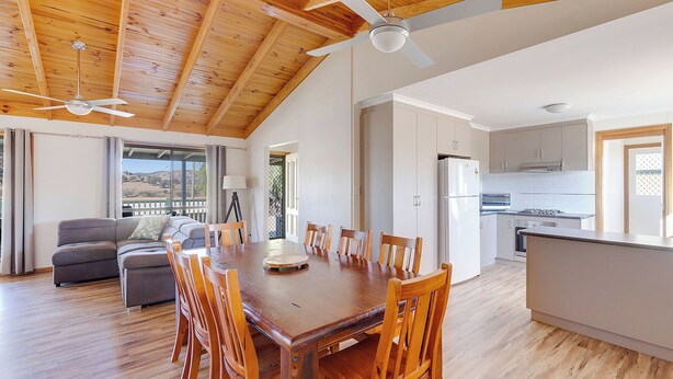 A spacious living area with a wooden dining table, chairs, a sofa, and a ceiling fan. - Reflections Grabine Lakeside - Holiday Park (Bigga)