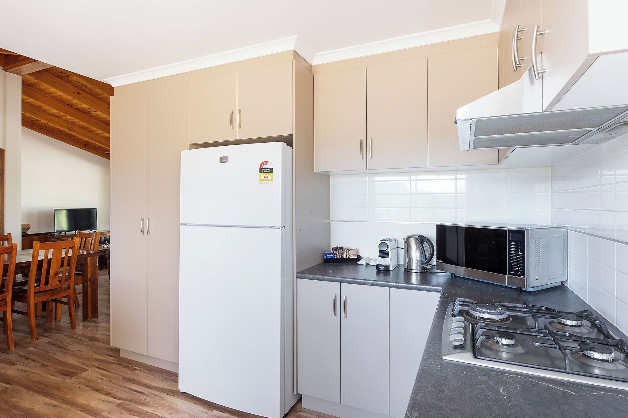 A compact kitchen with a refrigerator, microwave, stove, and wooden dining table with chairs.